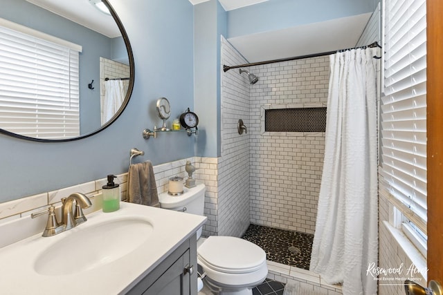 bathroom with toilet, tiled shower, vanity, and tile walls