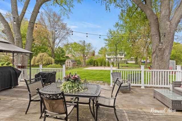 wooden deck with a storage shed, a gazebo, grilling area, a lawn, and an outbuilding