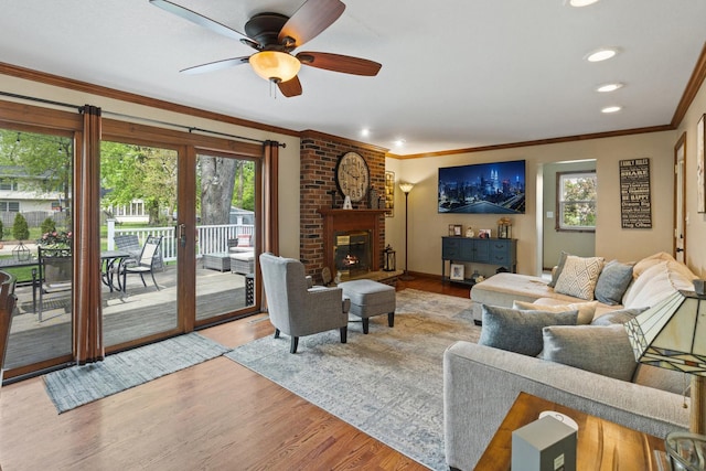 living area featuring wood finished floors, crown molding, ceiling fan, a brick fireplace, and recessed lighting