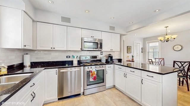 kitchen with stainless steel appliances, a peninsula, a chandelier, tasteful backsplash, and white cabinetry