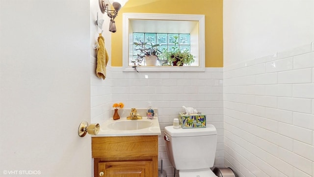 half bathroom featuring vanity, toilet, and tile walls