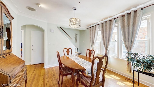 dining space featuring arched walkways, plenty of natural light, light wood-style flooring, and baseboards