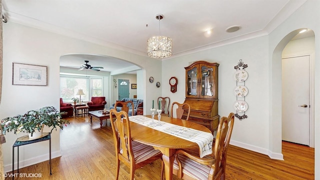 dining area with arched walkways, wood finished floors, a ceiling fan, and baseboards