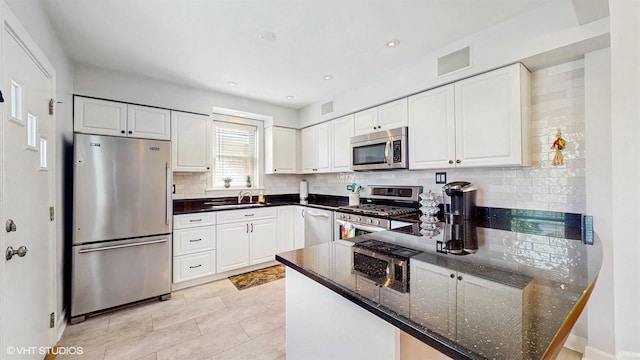 kitchen with stainless steel appliances, a peninsula, backsplash, white cabinets, and a sink