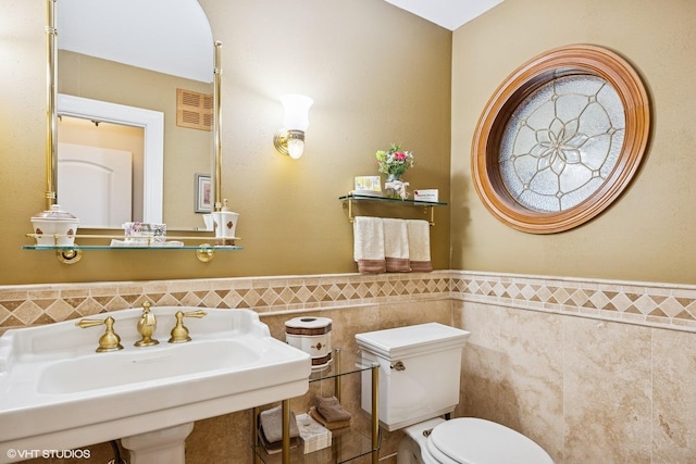 bathroom featuring tile walls, a sink, toilet, and wainscoting