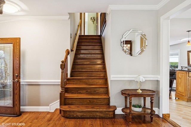 stairway with wood finished floors, ornamental molding, and baseboards