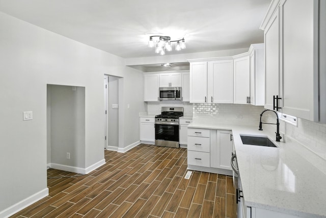kitchen featuring stainless steel appliances, a sink, tasteful backsplash, baseboards, and white cabinetry