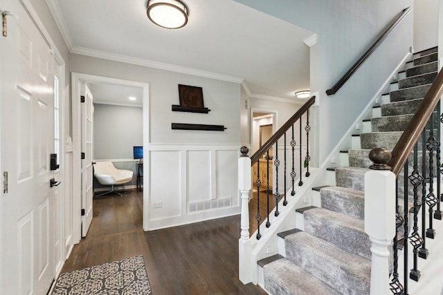 entrance foyer featuring ornamental molding, stairs, dark wood finished floors, wainscoting, and a decorative wall