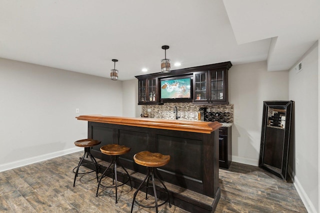 indoor wet bar featuring backsplash, dark wood-style flooring, baseboards, recessed lighting, and hanging light fixtures