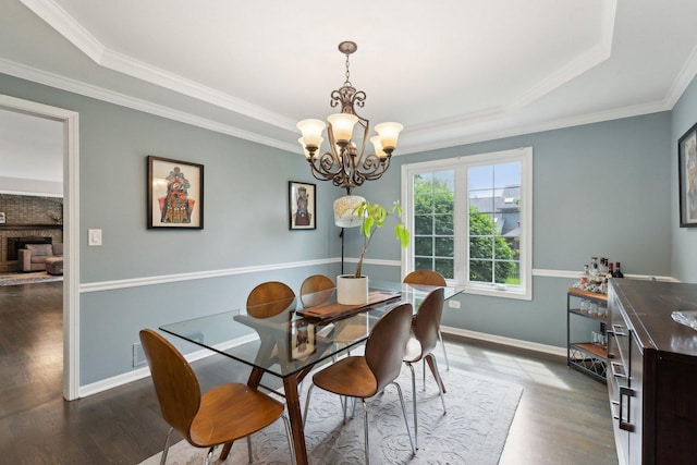 dining space featuring dark wood-style floors, a chandelier, a tray ceiling, baseboards, and crown molding