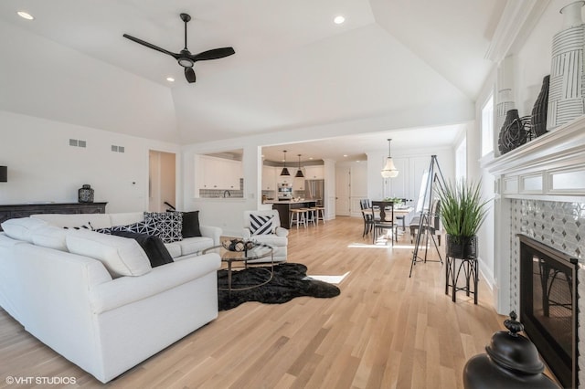 living room with high vaulted ceiling, a fireplace, visible vents, ceiling fan, and light wood-style floors