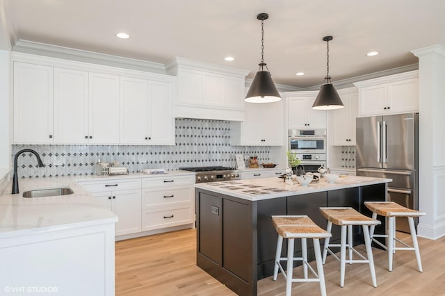kitchen featuring a sink, stainless steel appliances, a kitchen breakfast bar, pendant lighting, and white cabinets