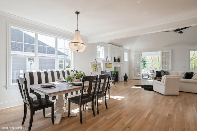 dining space featuring light wood-type flooring, a fireplace, an inviting chandelier, crown molding, and baseboards