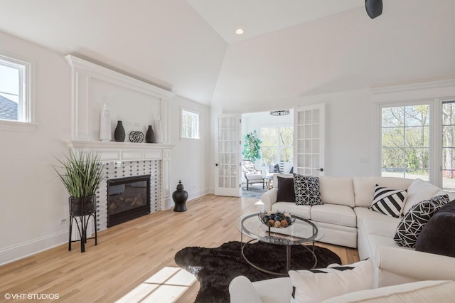 living area with baseboards, high vaulted ceiling, a tiled fireplace, and wood finished floors