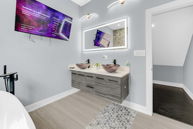 full bathroom featuring double vanity, wood finished floors, baseboards, and a sink