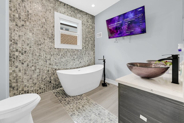 bathroom with toilet, wood finished floors, vanity, visible vents, and a freestanding tub