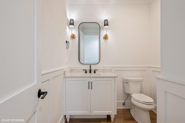 bathroom with toilet, wood finished floors, a decorative wall, wainscoting, and vanity