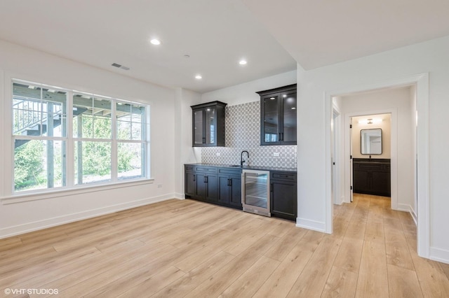 kitchen featuring beverage cooler, glass insert cabinets, light wood-style flooring, a sink, and visible vents
