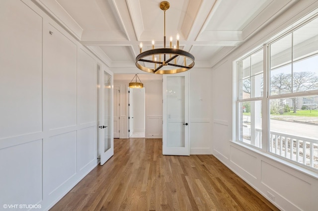 hall with a decorative wall, beam ceiling, light wood-type flooring, an inviting chandelier, and coffered ceiling