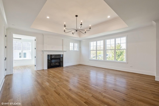 unfurnished living room with a raised ceiling, a chandelier, and wood finished floors