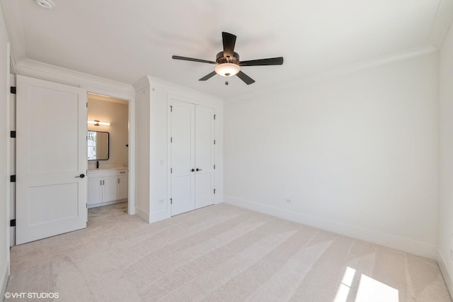 unfurnished bedroom featuring a closet, baseboards, ensuite bathroom, crown molding, and light carpet