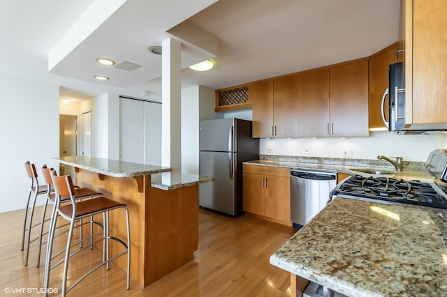 kitchen featuring appliances with stainless steel finishes, light wood-type flooring, a kitchen breakfast bar, light stone countertops, and brown cabinets