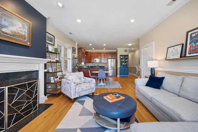 living area featuring crown molding, light wood-type flooring, recessed lighting, and a fireplace