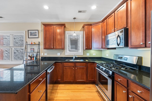 kitchen with appliances with stainless steel finishes, a sink, ornamental molding, light wood finished floors, and decorative light fixtures