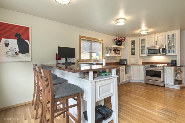 kitchen with appliances with stainless steel finishes, open shelves, a peninsula, and a breakfast bar area