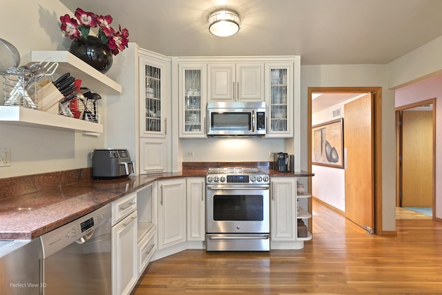 kitchen featuring appliances with stainless steel finishes, open shelves, wood finished floors, white cabinets, and glass insert cabinets
