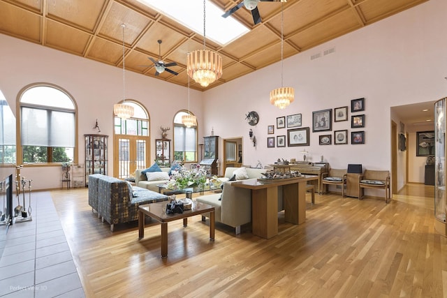 living room featuring ceiling fan, coffered ceiling, a chandelier, light wood-type flooring, and a towering ceiling