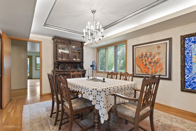 dining space with a chandelier, light wood-style flooring, a raised ceiling, and baseboards