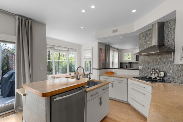 kitchen with stainless steel appliances, wall chimney exhaust hood, a sink, an island with sink, and plenty of natural light