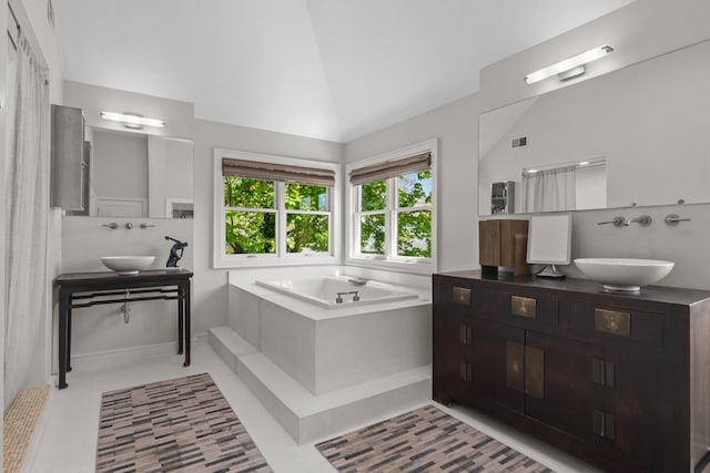 full bathroom with tile patterned flooring, a bath, two vanities, and vaulted ceiling