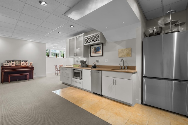 kitchen featuring appliances with stainless steel finishes, a sink, a drop ceiling, baseboards, and glass insert cabinets