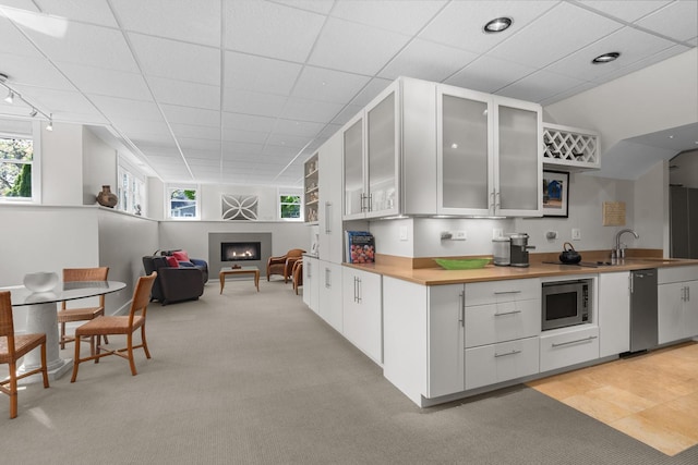 kitchen with stainless steel microwave, a warm lit fireplace, white cabinetry, healthy amount of natural light, and a drop ceiling