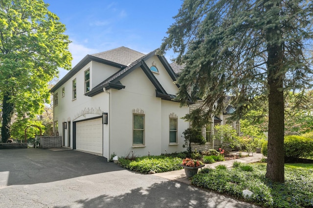 view of side of home featuring stucco siding, driveway, an attached garage, and a shingled roof