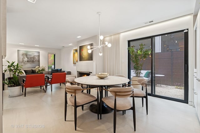 dining space featuring a warm lit fireplace and a chandelier