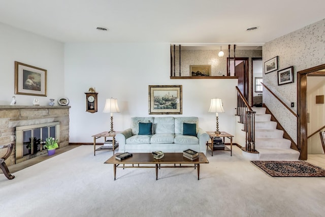 carpeted living room featuring a stone fireplace, stairs, baseboards, and wallpapered walls