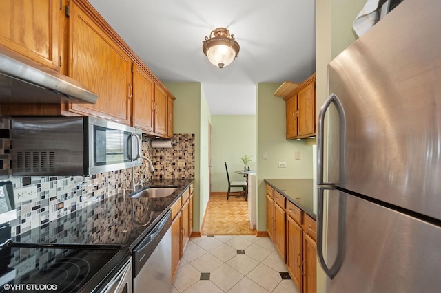 kitchen with stainless steel appliances, a sink, backsplash, and dark stone counters