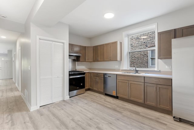 kitchen featuring stainless steel appliances, a sink, light wood-style flooring, under cabinet range hood, and light countertops