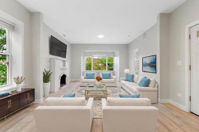 living area featuring healthy amount of natural light, light wood finished floors, baseboards, a brick fireplace, and recessed lighting