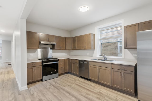 kitchen with stainless steel appliances, a sink, light wood finished floors, and light countertops