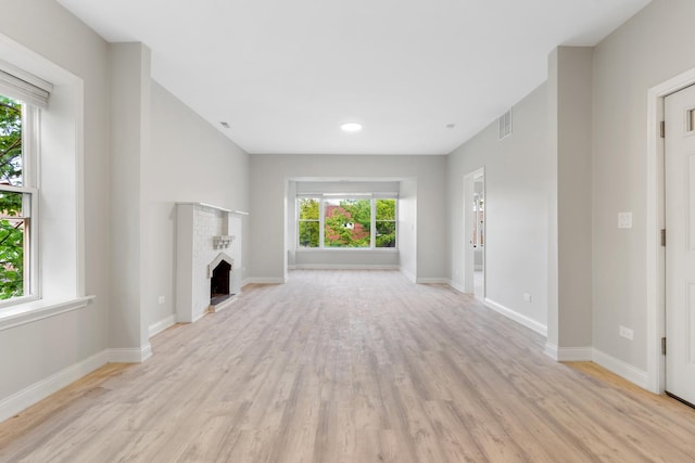unfurnished living room featuring plenty of natural light, light wood-type flooring, baseboards, a brick fireplace, and recessed lighting