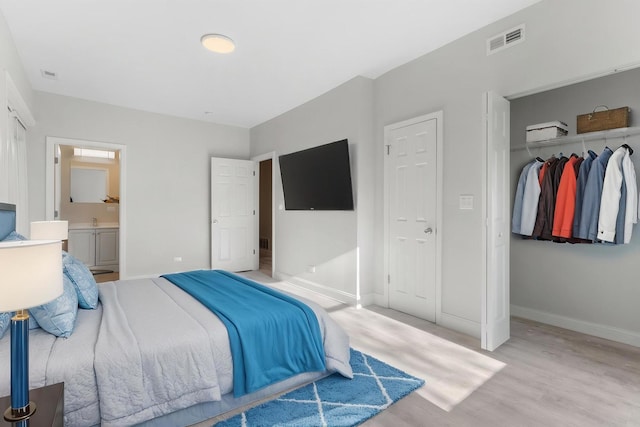 bedroom featuring a closet, light wood-style floors, baseboards, connected bathroom, and a sink