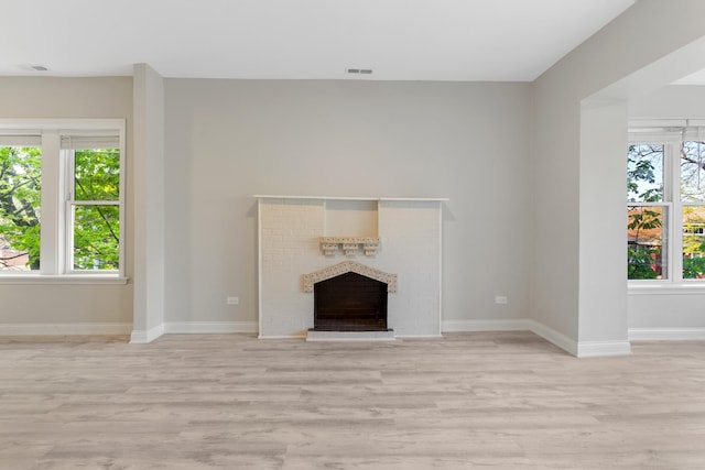 unfurnished living room featuring healthy amount of natural light, light wood-style floors, a fireplace, and baseboards