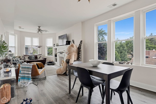 dining space with wood finished floors, visible vents, a fireplace, ceiling fan, and baseboards