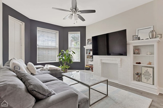 living area featuring baseboards, a fireplace, ceiling fan, and wood finished floors