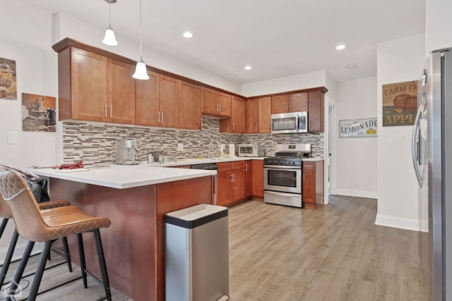 kitchen with a peninsula, stainless steel appliances, pendant lighting, backsplash, and light wood-style floors