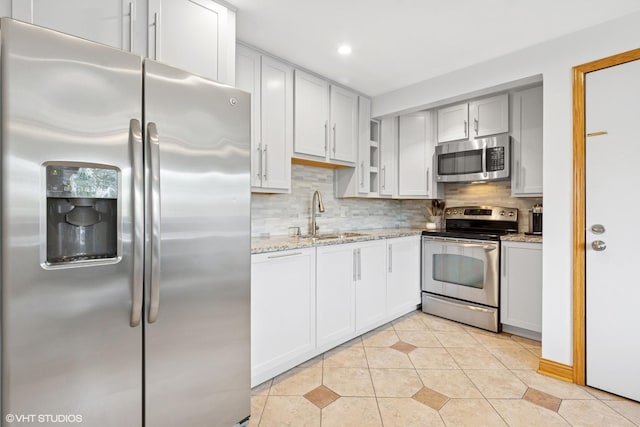kitchen with stainless steel appliances, a sink, tasteful backsplash, light stone counters, and recessed lighting